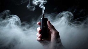 A hand holding a black vape device releasing vapor into the air with dark background, representing the hidden dangers of vaping.